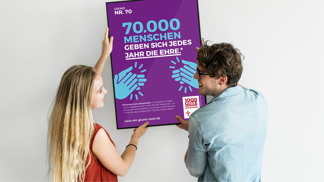 Ein junger Mann und eine junge Frau hängen das Plakat mit dem Ehrenamtsmotiv der Initiative 1000 gute Gründe auf